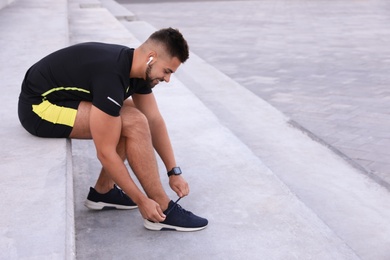 Young man with wireless headphones listening to music on stairs. Space for text