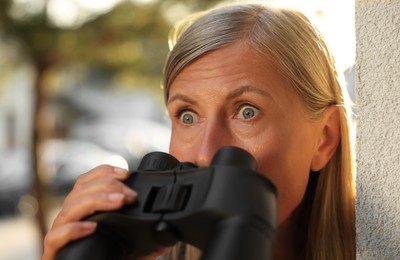 Photo of Concept of private life. Curious senior woman with binoculars spying on neighbours outdoors, closeup