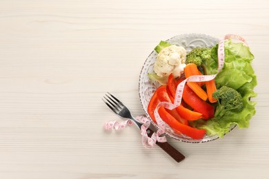 Photo of Healthy diet. Plate of fresh vegetables, measuring tape and fork on light wooden table, top view. Space for text