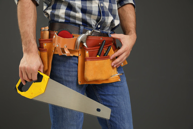 Photo of Carpenter with tool belt and hand saw on dark background, closeup