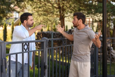 Photo of Angry neighbours having argument near fence outdoors