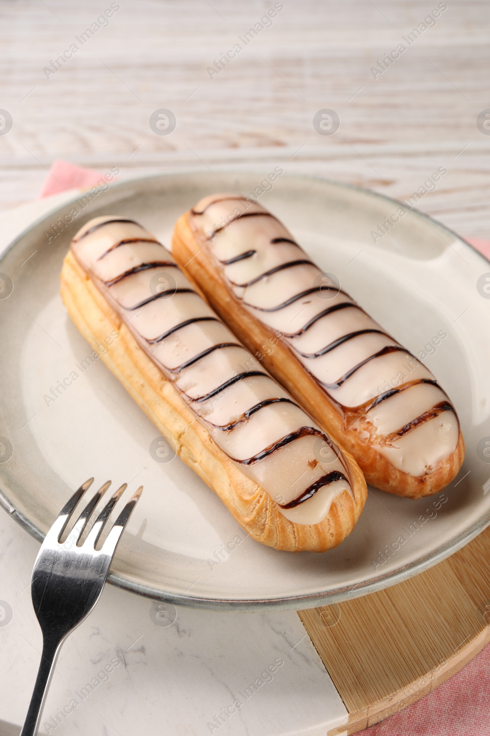 Photo of Tasty glazed eclairs served on table, closeup