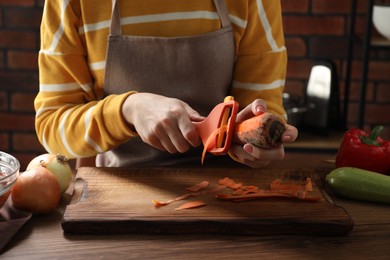 Photo of Woman peeling fresh carrot at wooden table indoors, closeup