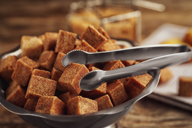 Photo of Brown sugar cubes in metal bowl on wooden table, closeup