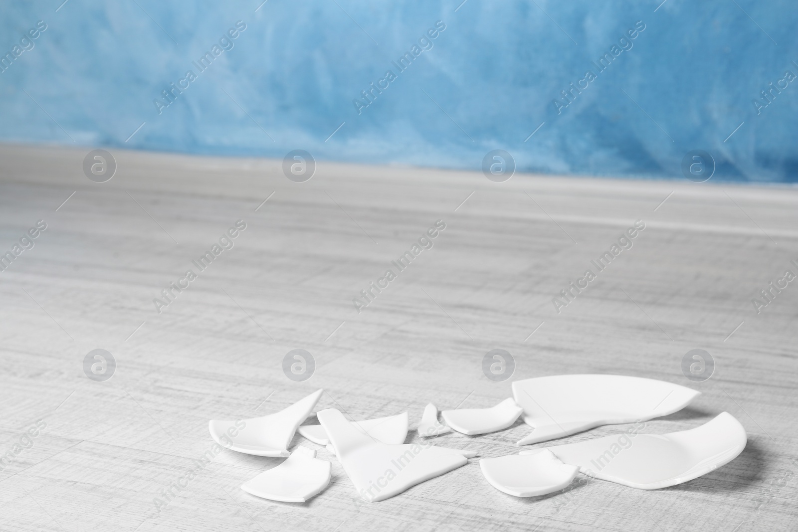 Photo of Pieces of broken ceramic plate on white wooden floor indoors, space for text