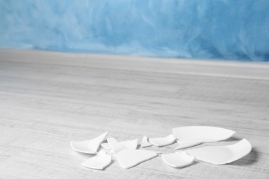 Photo of Pieces of broken ceramic plate on white wooden floor indoors, space for text