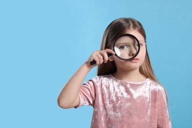 Photo of Cute little girl looking through magnifier glass on light blue background. Space for text