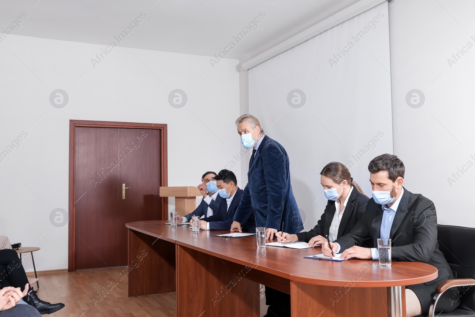 Photo of Business conference. People with protective masks listening to speaker report