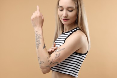 Tattooed woman applying cream onto her arm on beige background