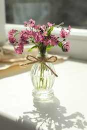 Beautiful pink forget-me-not flowers in glass bottle on window sill