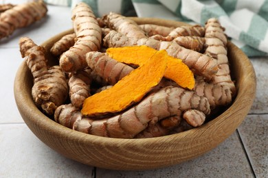 Photo of Bowl with whole and cut turmeric roots on table, closeup