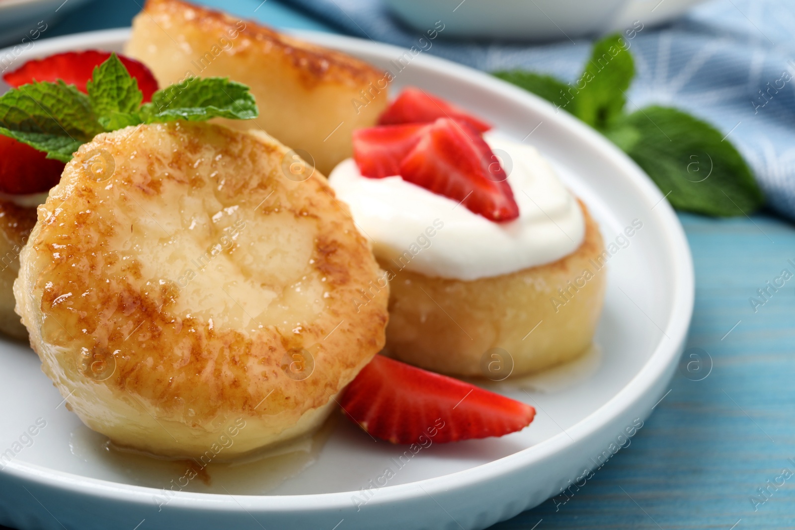 Photo of Delicious cottage cheese pancakes with strawberries, honey and sour cream on light blue wooden table, closeup