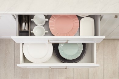 Photo of Clean plates, bowls and cutlery in drawers indoors, top view