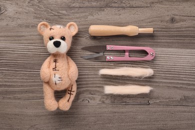 Photo of Needle felted bear, wool and different tools on wooden table, flat lay