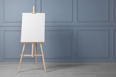 Photo of Wooden easel with blank canvas near grey wall indoors. Space for text