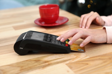 Photo of Woman using card machine for non cash payment at table, closeup