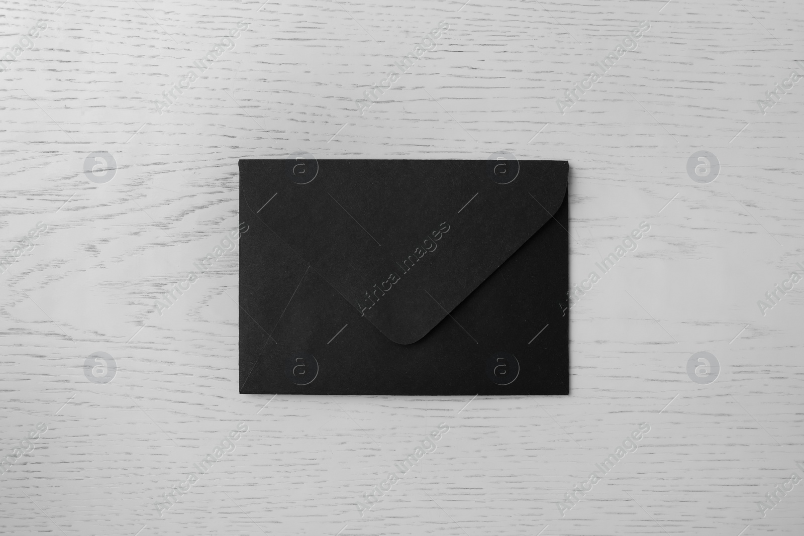 Photo of Black paper envelope on white wooden background, top view
