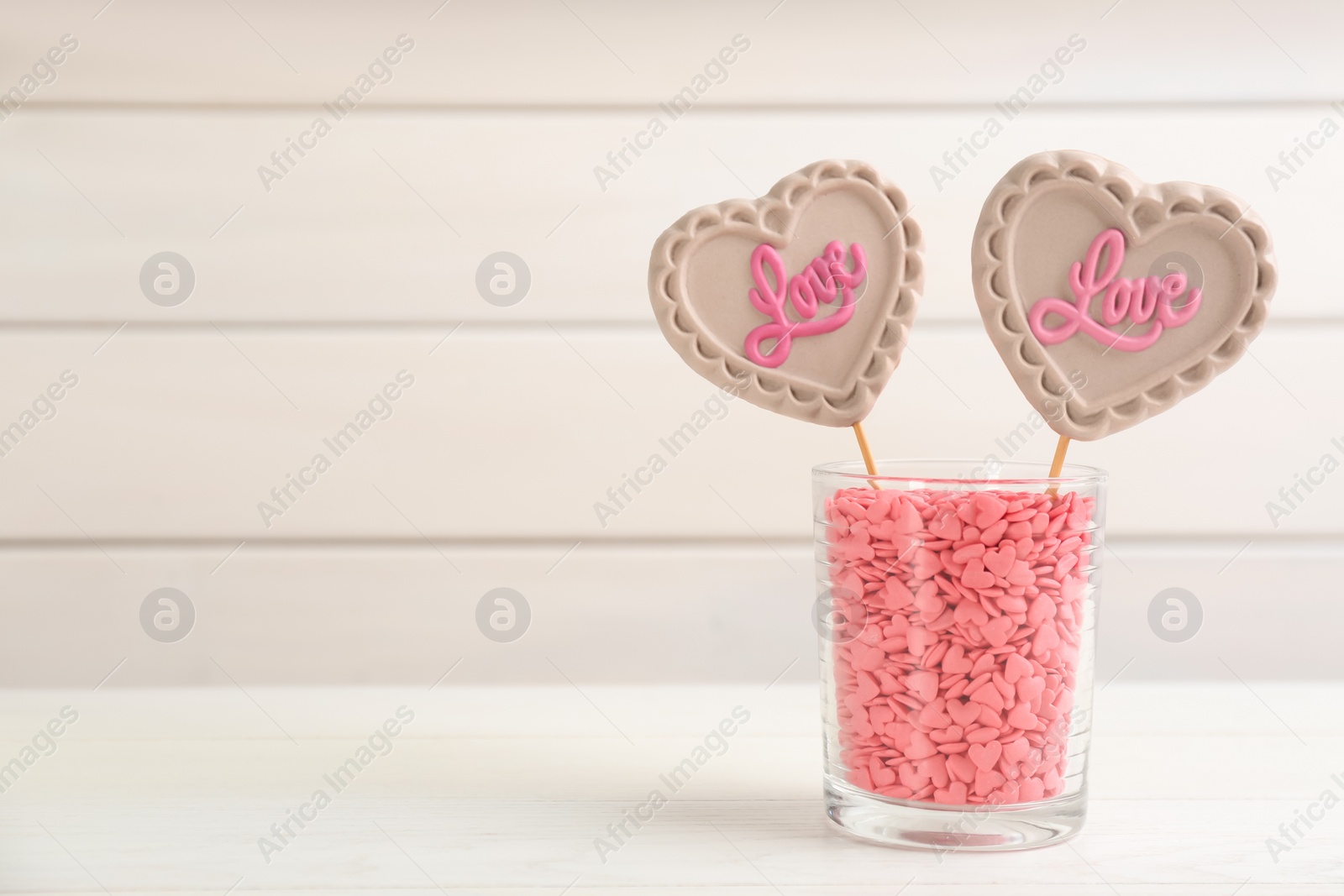 Photo of Heart shaped lollipops made of chocolate with sprinkles in cup on white table, space for text