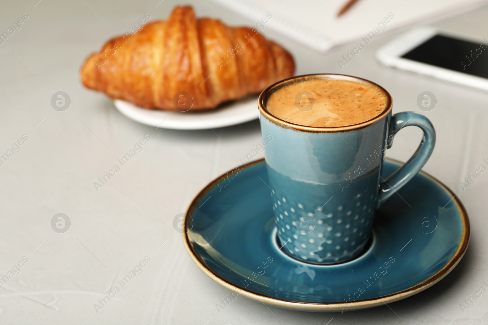 Photo of Cup of tasty aromatic coffee and croissant on grey table. Space for text