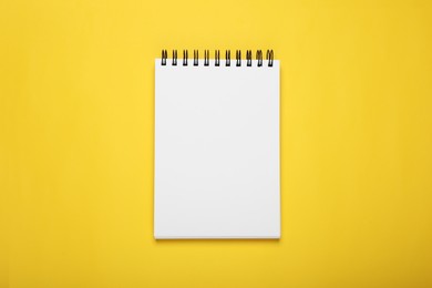 Blank office notebook on yellow background, top view