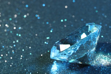 Photo of Beautiful dazzling diamond on light blue glitter background, closeup. Space for text
