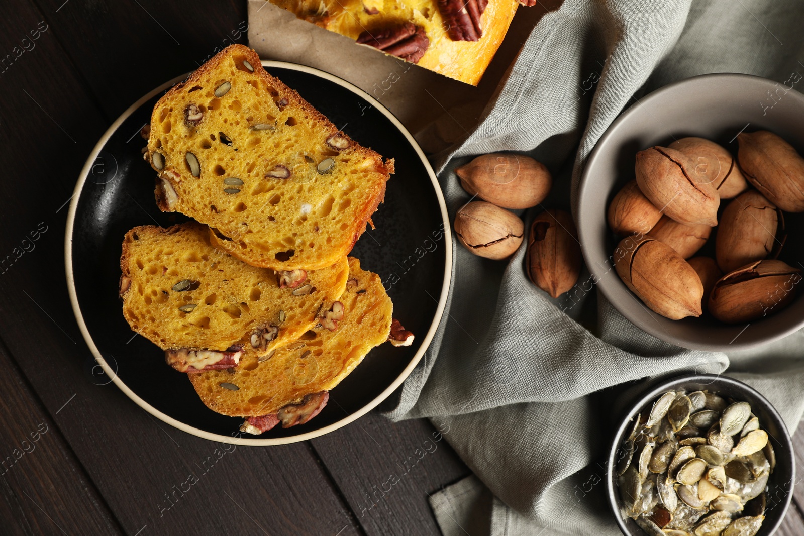 Photo of Delicious pumpkin bread with pecan nuts and seeds on wooden table, flat lay