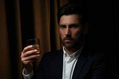 Photo of Man in suit holding glass of whiskey with ice cubes on brown background