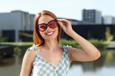 Beautiful smiling woman in sunglasses near river, space for text