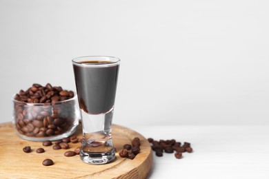 Photo of Shot glass of coffee liqueur and beans on white table, space for text