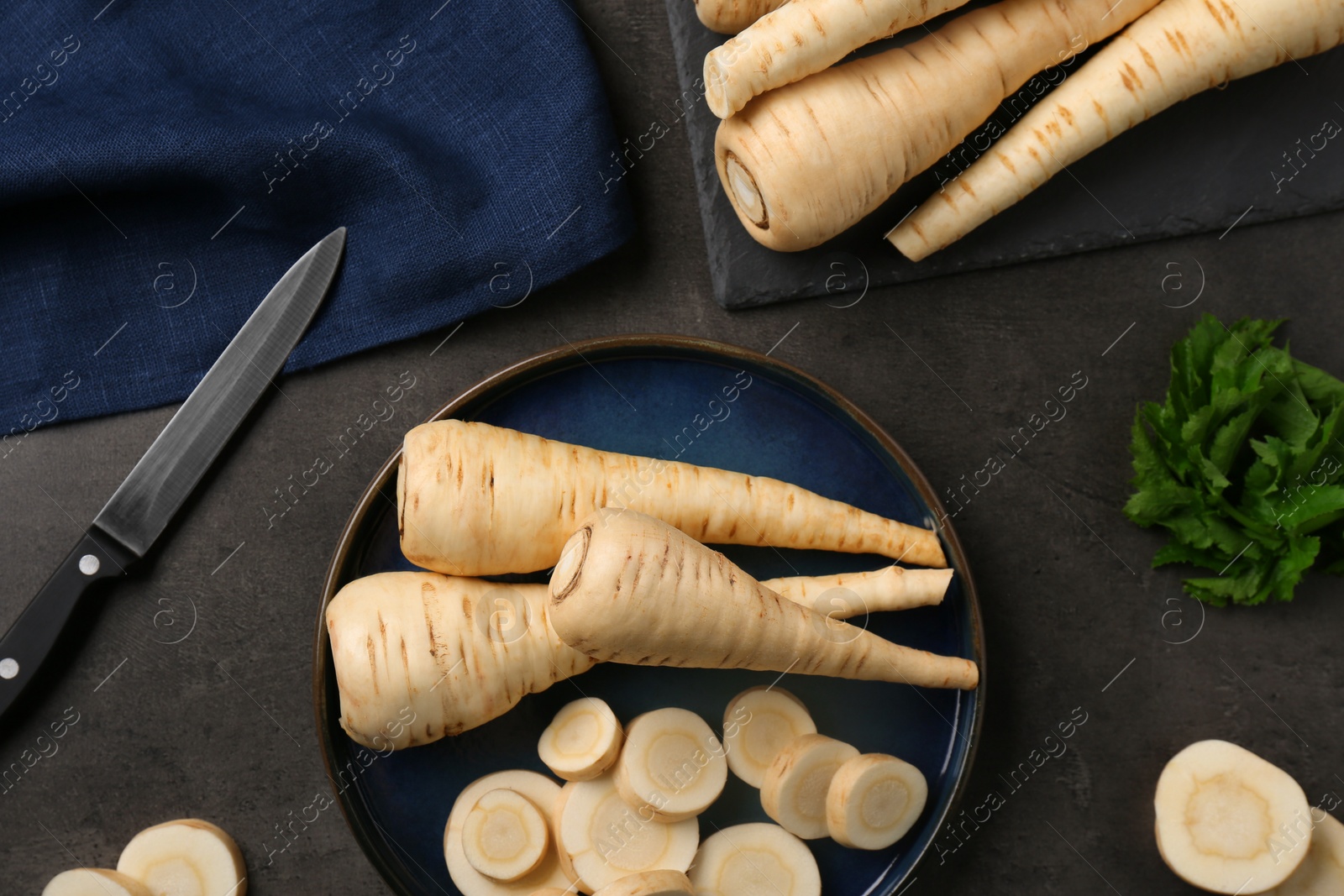 Photo of Whole and cut parsnips on black table, flat lay