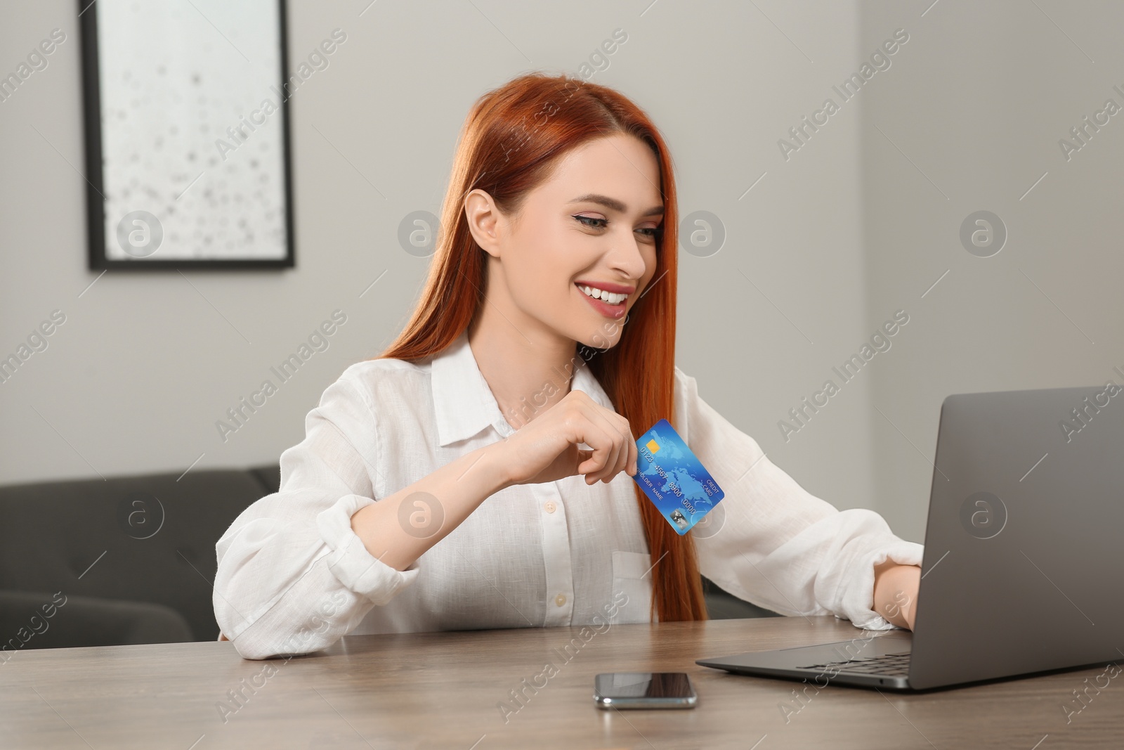 Photo of Happy woman with credit card using laptop for online shopping at wooden table in room