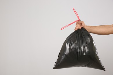 Photo of Man holding full garbage bag on light background, closeup. Space for text