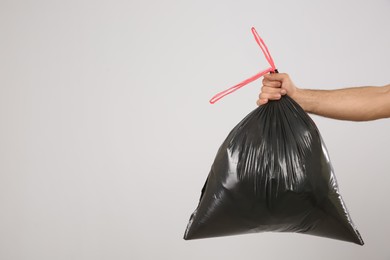 Man holding full garbage bag on light background, closeup. Space for text