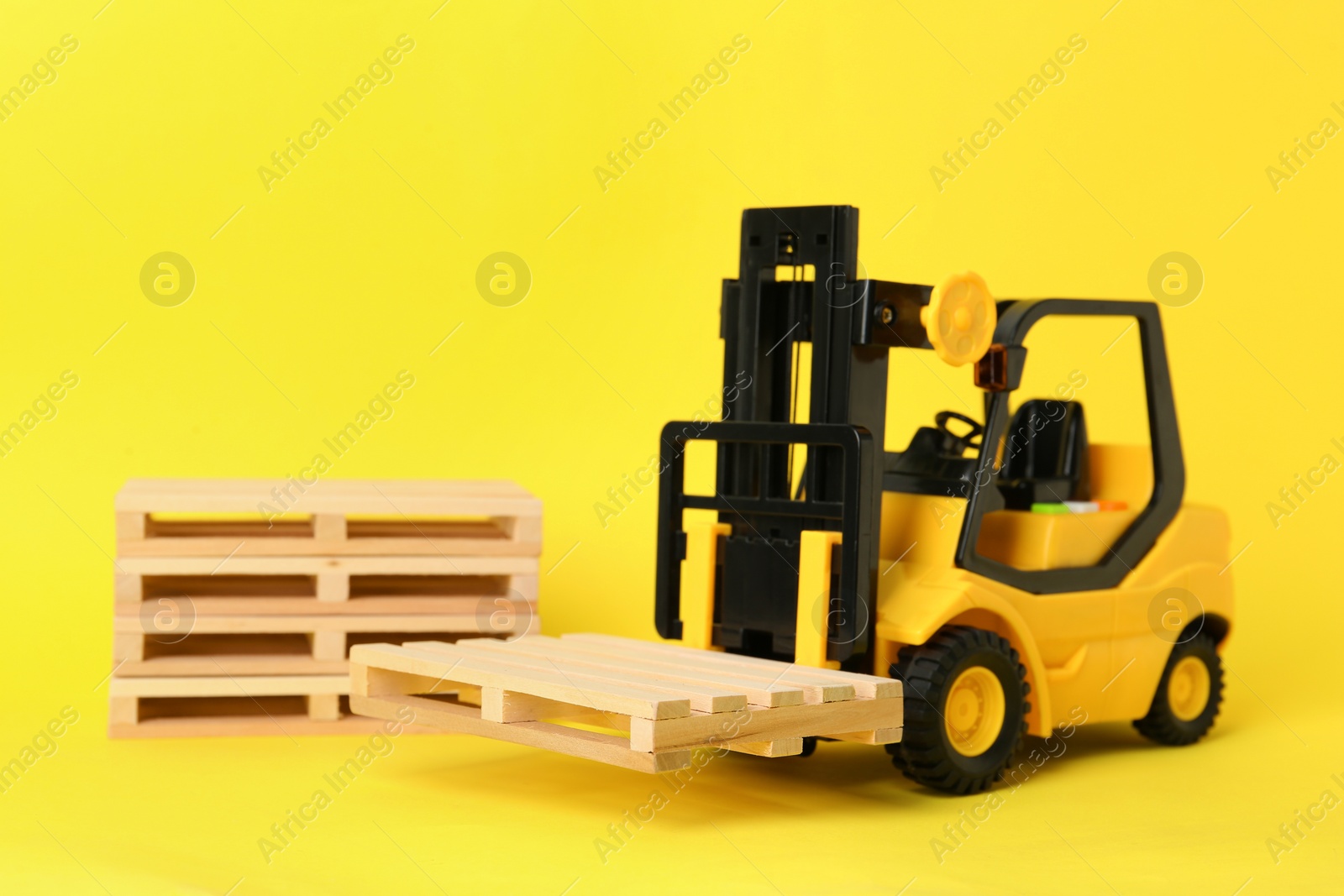 Photo of Toy forklift and wooden pallets on yellow background