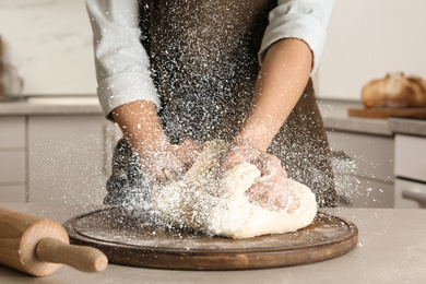 Image of Young woman kneading dough at table in kitchen, closeup