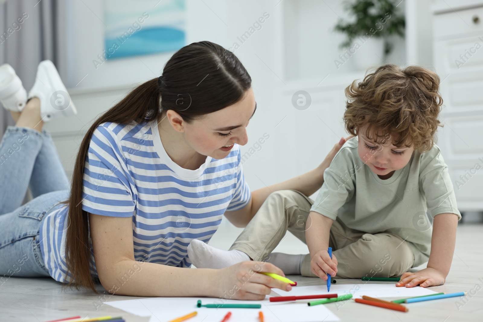 Photo of Mother and her little son drawing with colorful markers on floor at home