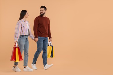 Happy couple with shopping bags on beige background. Space for text