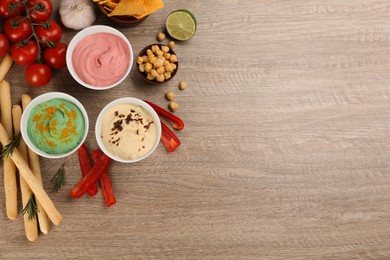 Photo of Different kinds of tasty hummus served with bread sticks on wooden table, flat lay. Space for text