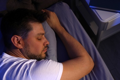 Photo of Handsome man sleeping on pillow in dark room at night, view from above. Bedtime