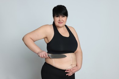 Photo of Obese woman with knife and marks on body against light background. Weight loss surgery