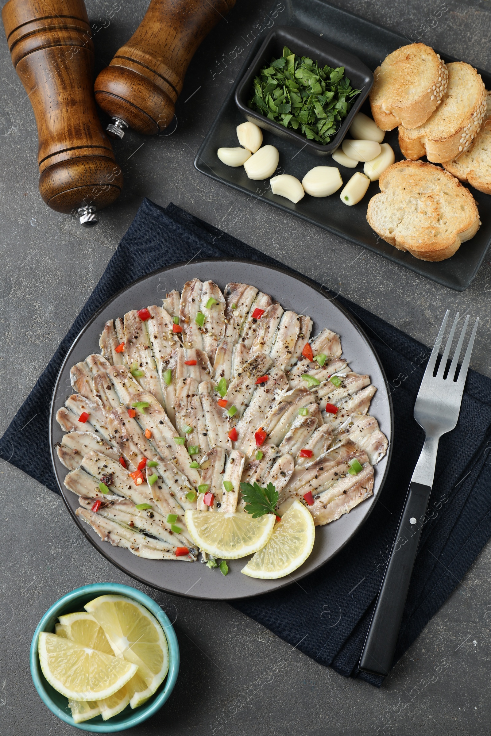 Photo of Tasty pickled anchovies served on grey textured table, flat lay