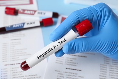 Photo of Scientist holding tube with blood sample and label Hepatitis A test near laboratory form, closeup