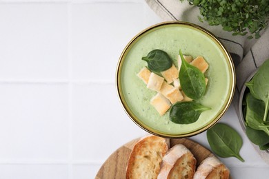 Delicious spinach cream soup with croutons in bowl on white tiled table, flat lay. Space for text