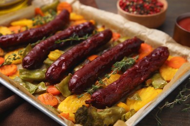 Baking tray with delicious smoked sausages and vegetables on table, closeup