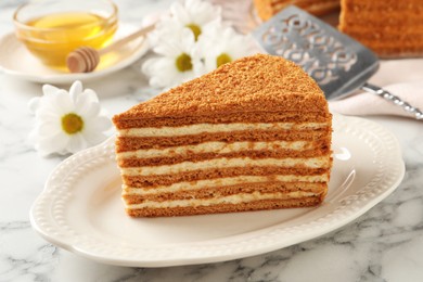 Slice of delicious layered honey cake served on white marble table, closeup