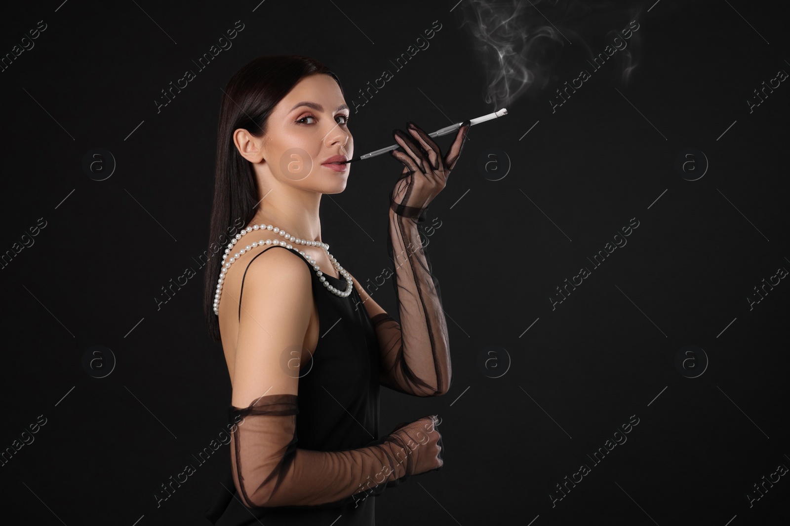 Photo of Woman using long cigarette holder for smoking on black background, space for text