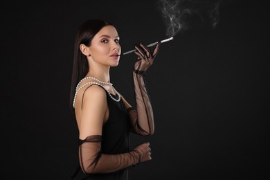 Woman using long cigarette holder for smoking on black background, space for text