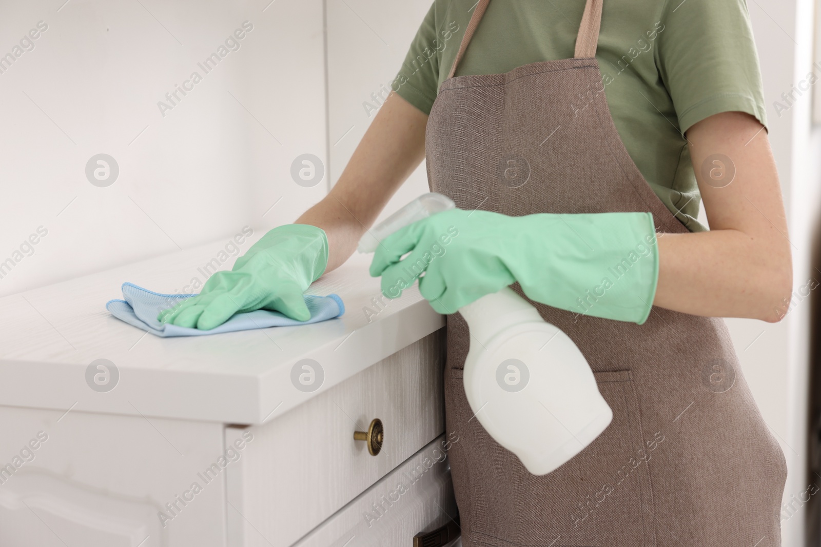 Photo of Woman with spray bottle and microfiber cloth cleaning white chest of drawers in room