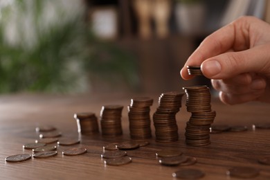 Woman stacking coins at wooden table indoors, closeup