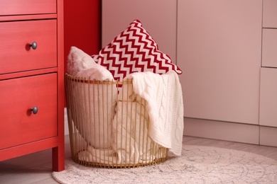 Basket with blanket and pillows near commode indoors